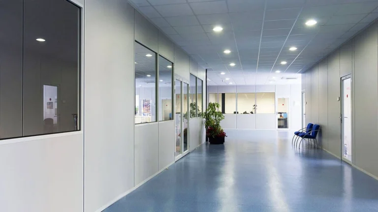 Couloir de bureaux bordé de cloisons semi-vitrées en kit, faux plafond lumineux et sol bleu