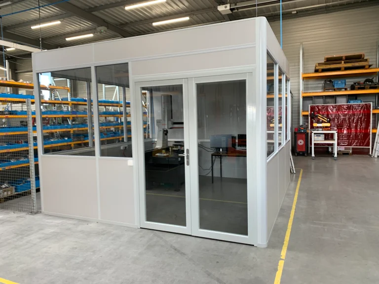 Cabine d’atelier en kit 4 faces à double porte vitrée, posée librement dans un entrepôt entre les rayonnages