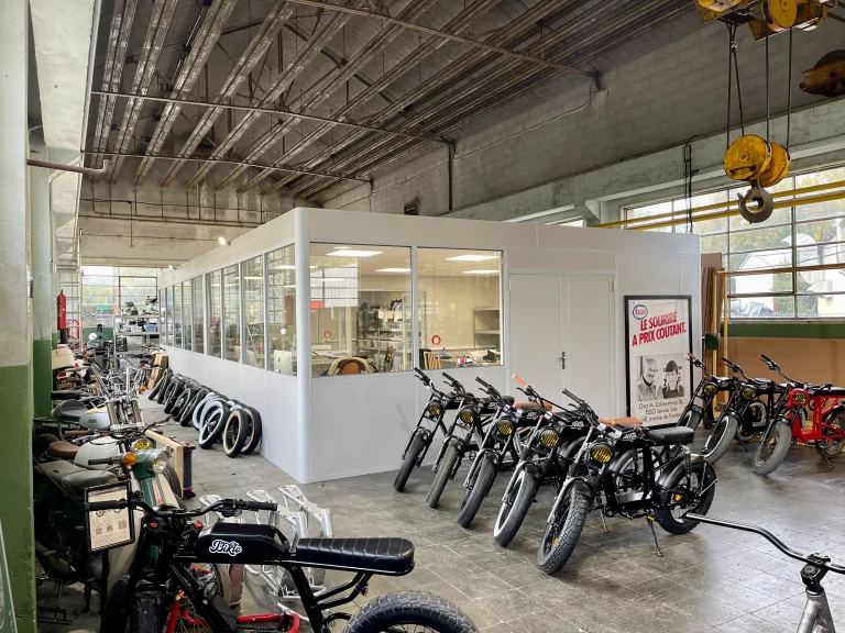 Cabine en kit semi-vitrée au fond de l’atelier d’un fabricant de vélos électriques, vélos alignés au premier plan