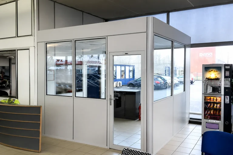 Cabine en kit vitrée construite en reprise d’angle sur deux murs, avec porte vitrée, dans un espace d’accueil