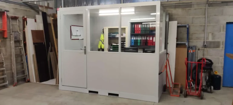 Bureau préfabriqué avec rayonnages d’archives, posé contre un mur en parpaings dans un local technique