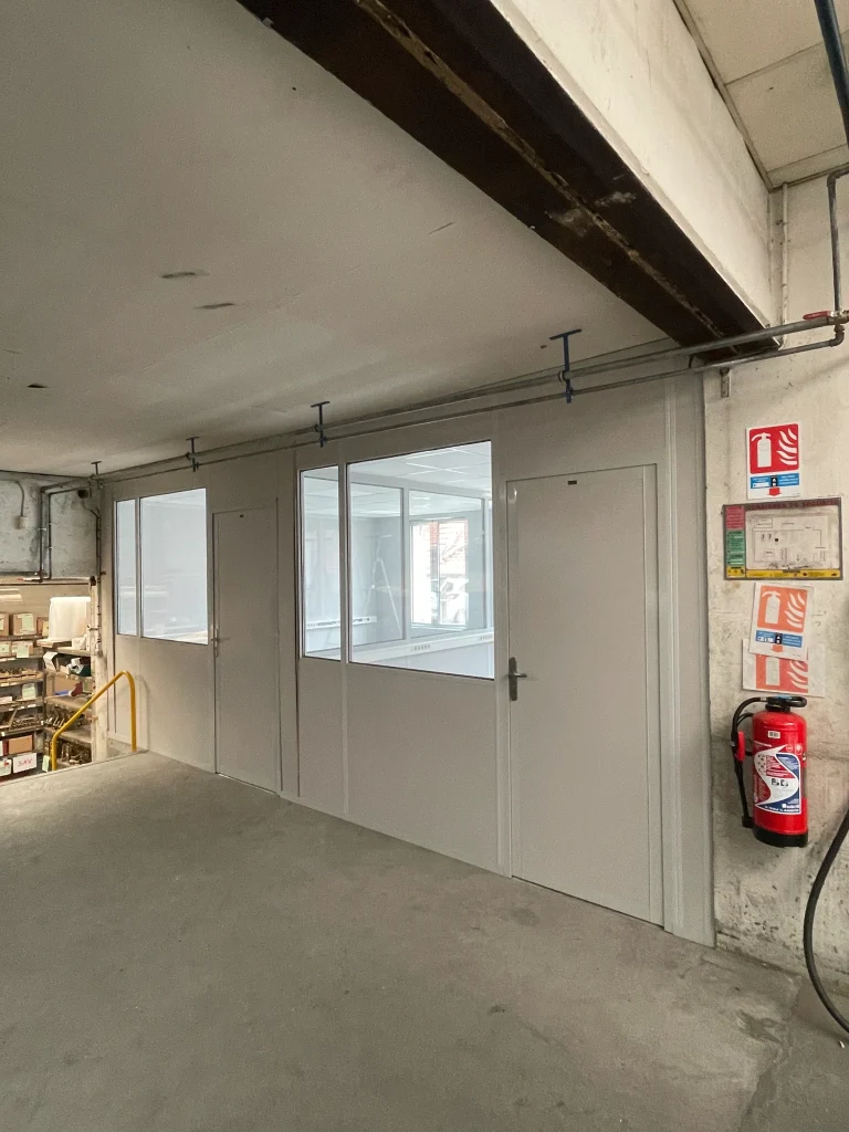 Cloison de bureau en kit semi-vitrée avec porte, installée dans un bâtiment industriel au sol béton