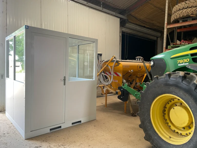 Bureau industriel préfabriqué dans un atelier de réparation de machines agricoles, à côté d’un tracteur