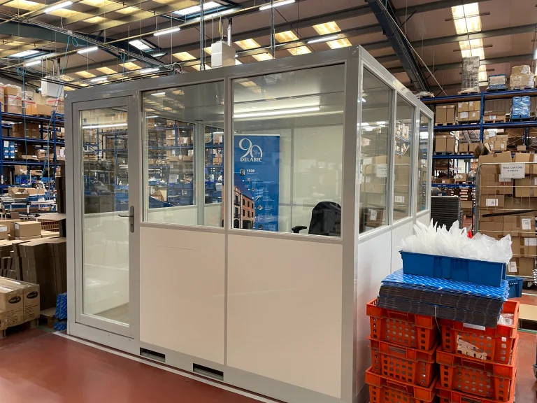 Bureau de magasinier vitré posé entre les rayonnages d’un stock de pièces