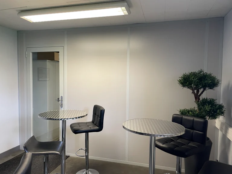Espace de pause fermé par une cloison pleine blanche avec porte vitrée, mange-debout et tabourets