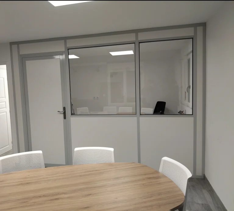 Salle de réunion fermée par une cloison de bureau en kit semi-vitrée avec porte, table ronde au premier plan